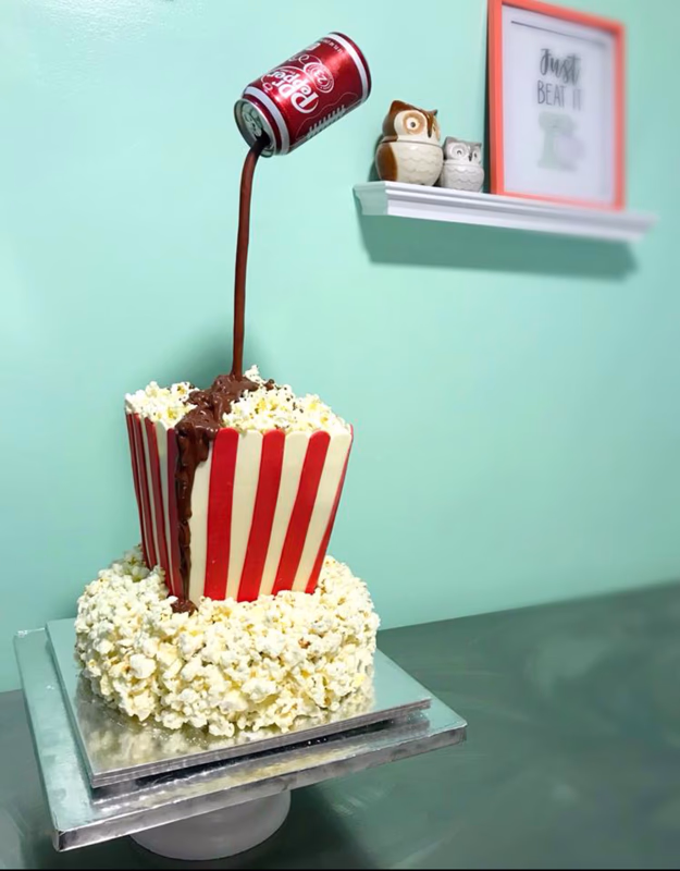 A fun cake featuring popular movie snacks like popcorn and soda.