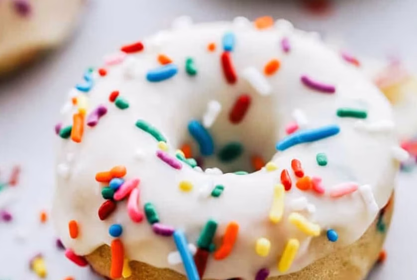 A fresh baked donut with white frosting and birthday sprinkles