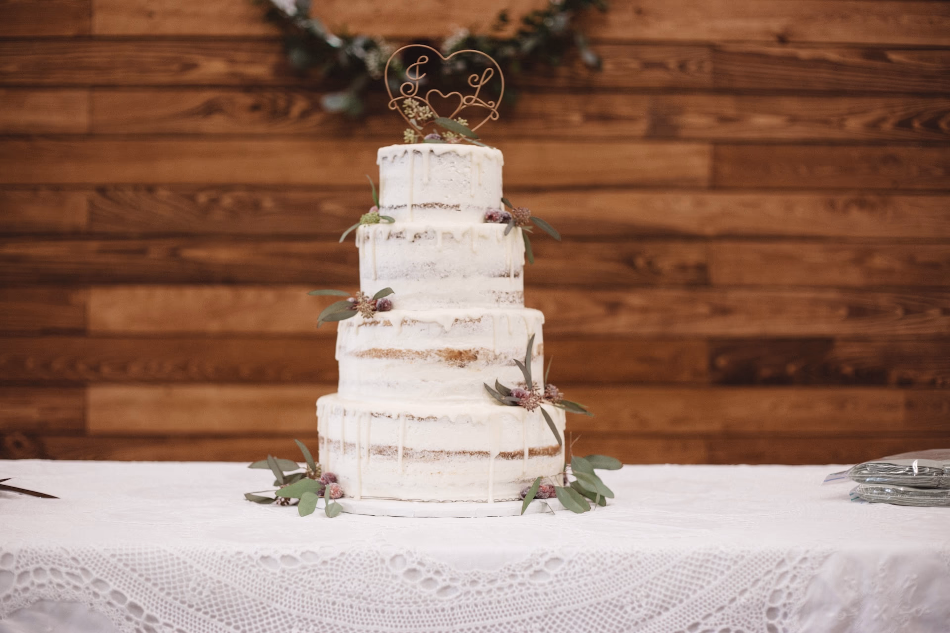 A four tiered wedding cake with white icing and cranberry and leaf accents.